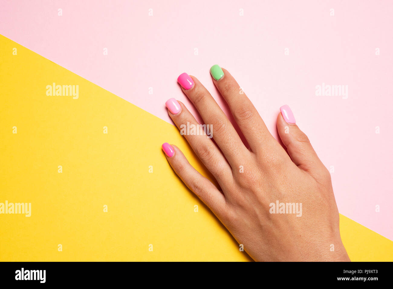 Nahaufnahme der Hand eines jungen kaukasischen Frau mit ihrem Fingernägel lackiert rosa und Hellgrün, rosa und gelben Hintergrund, mit einem leeren Raum o Stockfoto