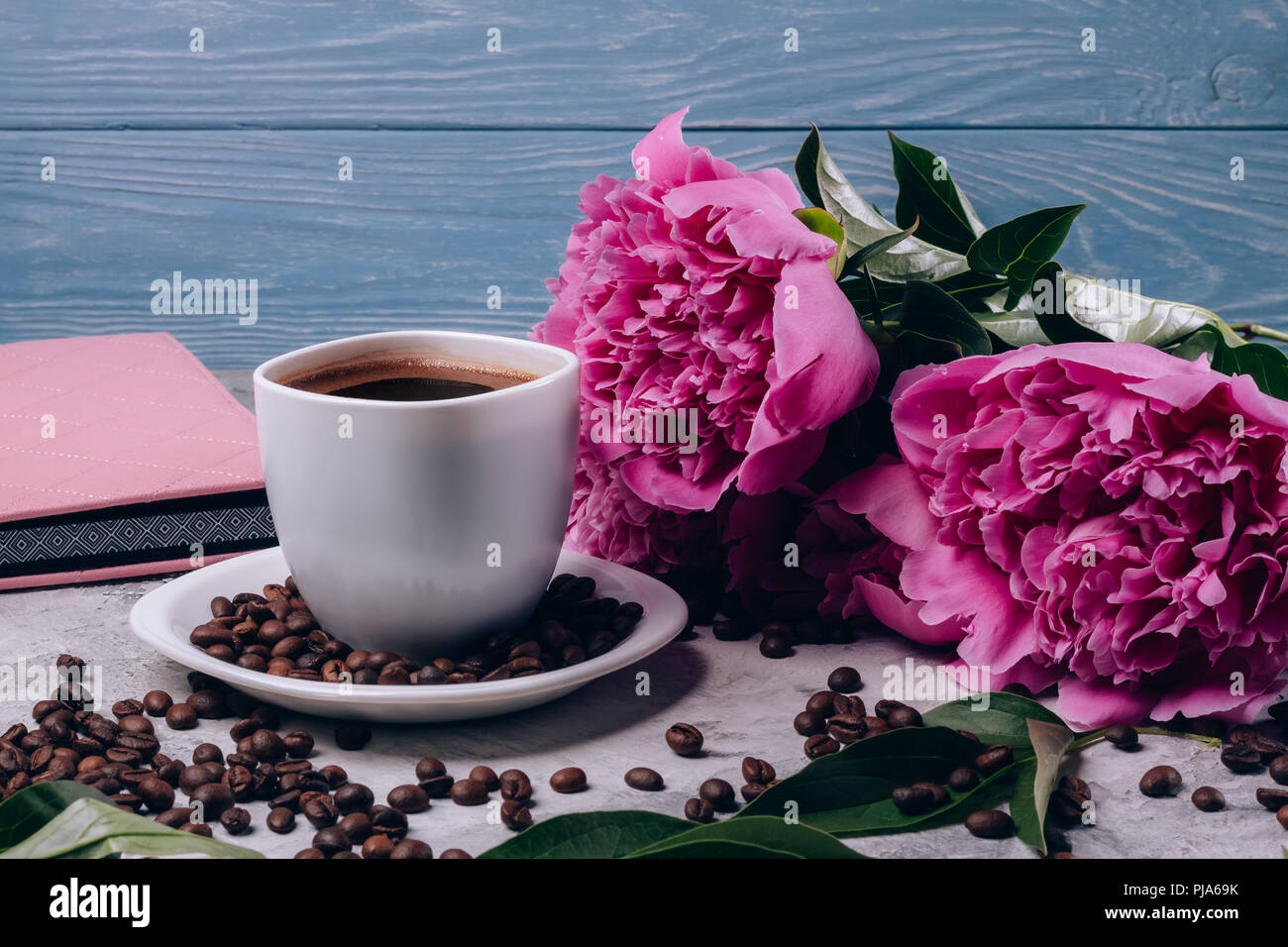 Schöne Päonien mit riesigen rosa Knospen auf den Tisch neben einer Tasse Kaffee auf einem blauen Hintergrund Stockfoto