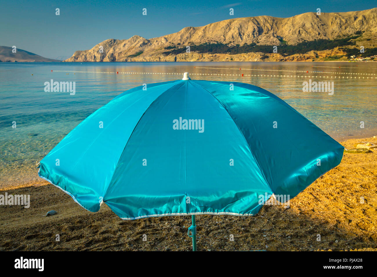 Ein einsamer Sonnenschirm am Strand bei Tagesanbruch am Wasser der Adria in Baska auf der Insel Krk Stockfoto