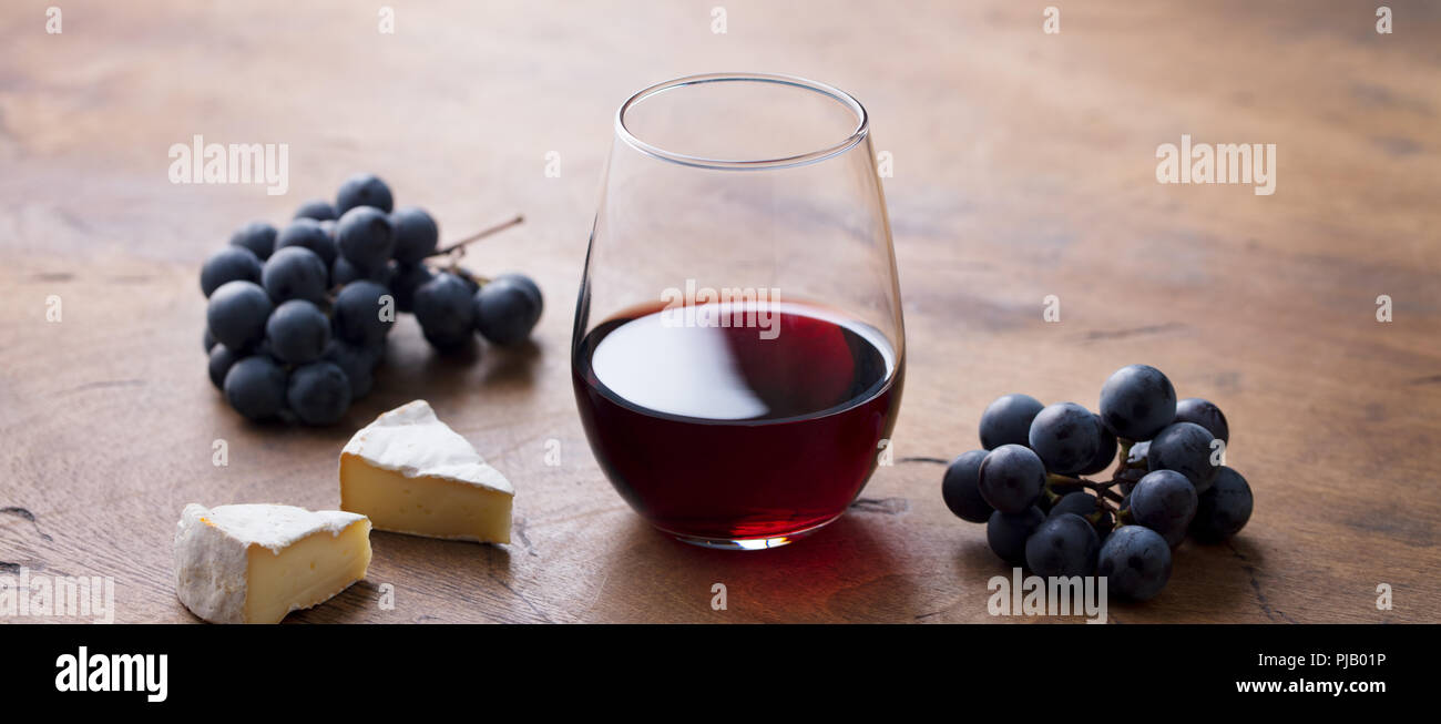 Glas Rotwein mit frischen Trauben und Käse auf dem Holztisch. Stockfoto