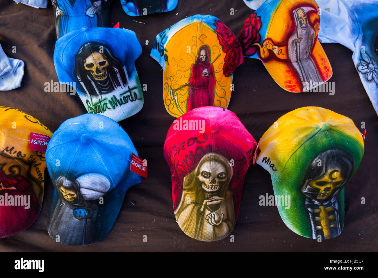 Bunte Baseball Caps, mit verschiedenen Santa Muerte Bilder (Heiligen Tod), werden auf der Straße während einer Pilgerreise in Mexiko City, Mexiko verkauft. Stockfoto