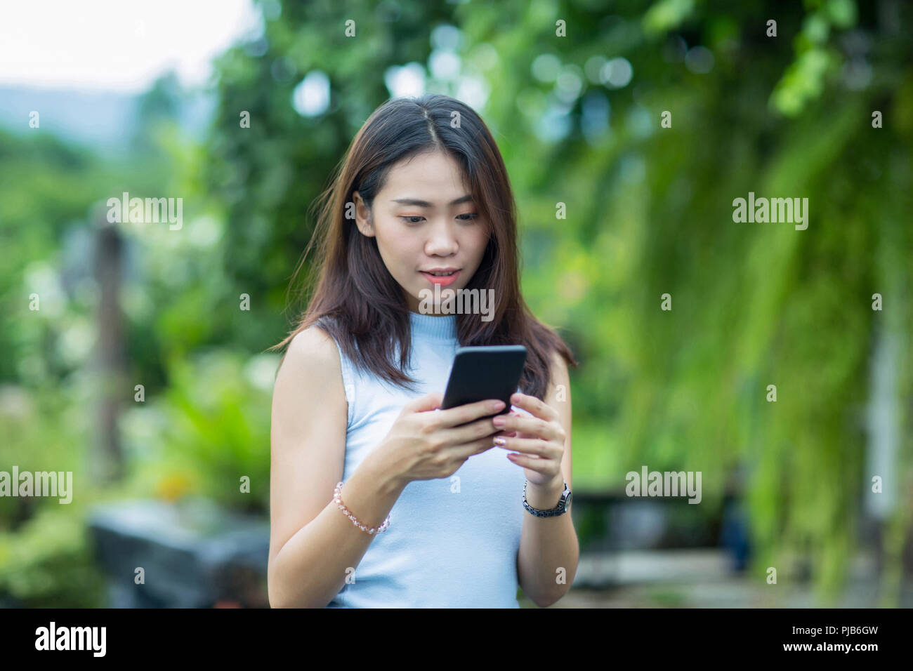 Asiatische Mädchen im Garten mit ihrem Handy entspannen und Kontrolle der Text Stockfoto