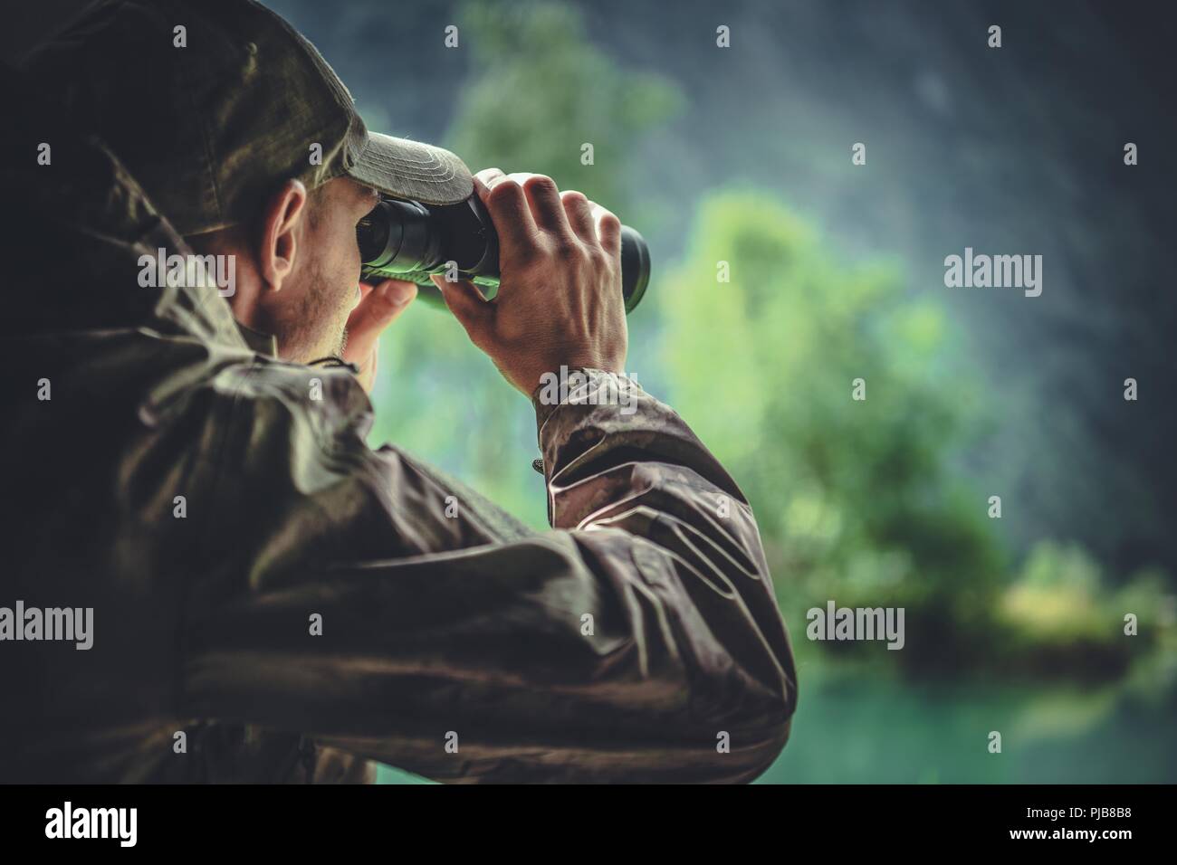 Kaukasische Jäger in der Maskierung Camouflage Uniform mit Fernglas. Hunter Spotting Spiel. Wilderer oder Soldat Kleidung. Stockfoto