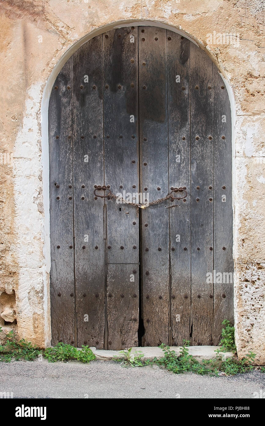 Rustikale braun gewölbten alte Holztür mit Vorhängeschloss auf Gebäude aus Stein auf Mallorca, Spanien. Stockfoto