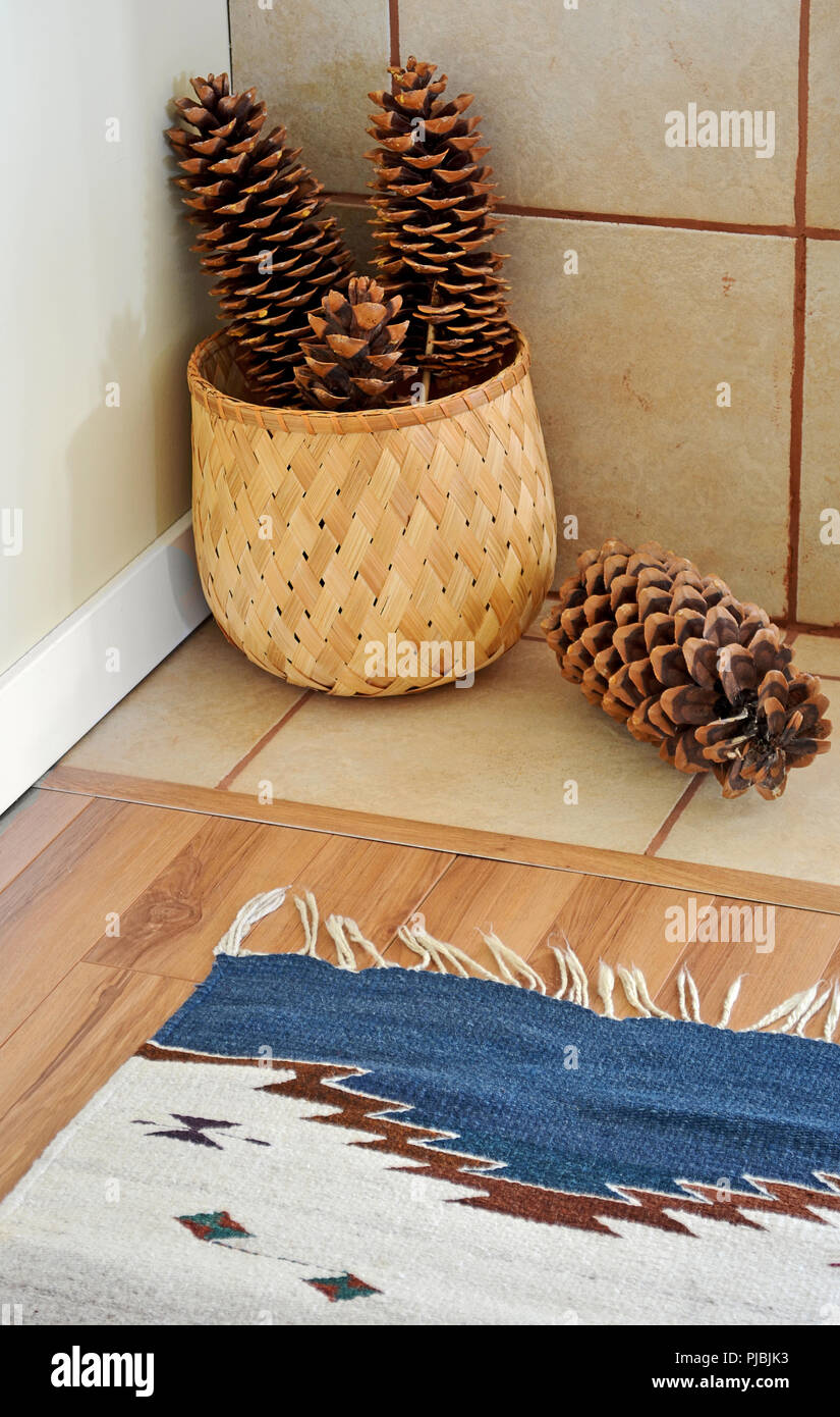 Große Zucker Tannenzapfen gewebt Bambus Korb und bunten handgewebten Teppich einen warmen rustikalen natürlichen Akzent in einer Ecke eines Zimmer hinzufügen Stockfoto