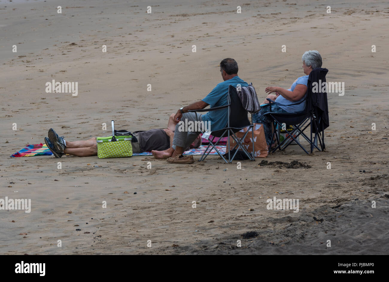 Eine Familie sitzt auf einem ansonsten leeren Strand in Klappstühle an einem bewölkten Sommertag. Stockfoto