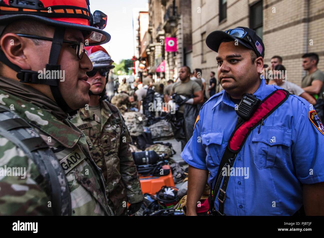 Armee finden Spc. Jason Delgado, 328 unterstützen Hosptial, spricht mit einem Sanitäter mit der New Yorker Feuerwehr, bevor Sie eine simulierte chemischen Angriff in Manhattan, New York, Juli, 10, 2018. Diese Soldaten sind Teil eines National Response Element, das mit der zivilen Behörden manpower, Fahrzeuge und Ausrüstung zu bieten medizinische Leistungen zu erbringen sowie chemische, biologische und radiologische clean up - Fähigkeiten, die in der hohen Nachfrage im Falle einer Katastrophe oder angreifen würde. Stockfoto