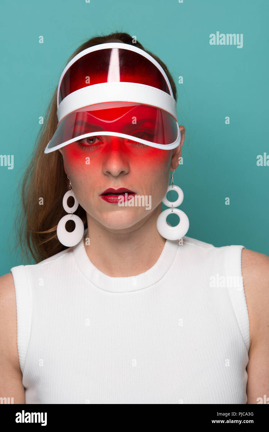 Ein rotes Haar kaukasische Frau mit Pferdeschwanz, trug einen Mod 60s style Ohrringe in einer roten Schirmmütze posiert, eine Nahaufnahme Porträt. Stockfoto