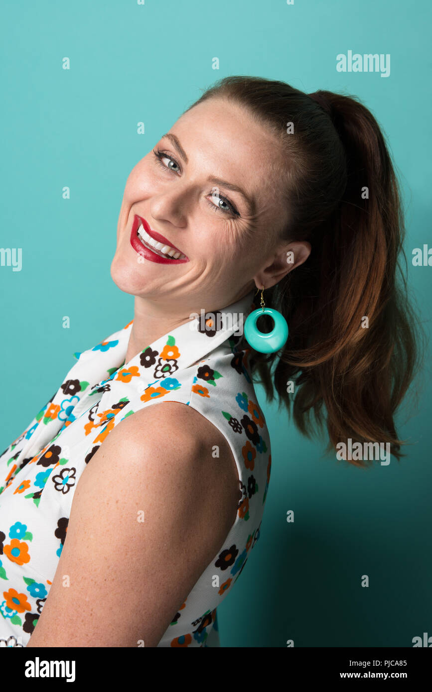 Ein rotes Haar kaukasische Frau mit Pferdeschwanz, trug einen Mod 60s style Ohrringe posiert, eine Nahaufnahme Porträt. Stockfoto