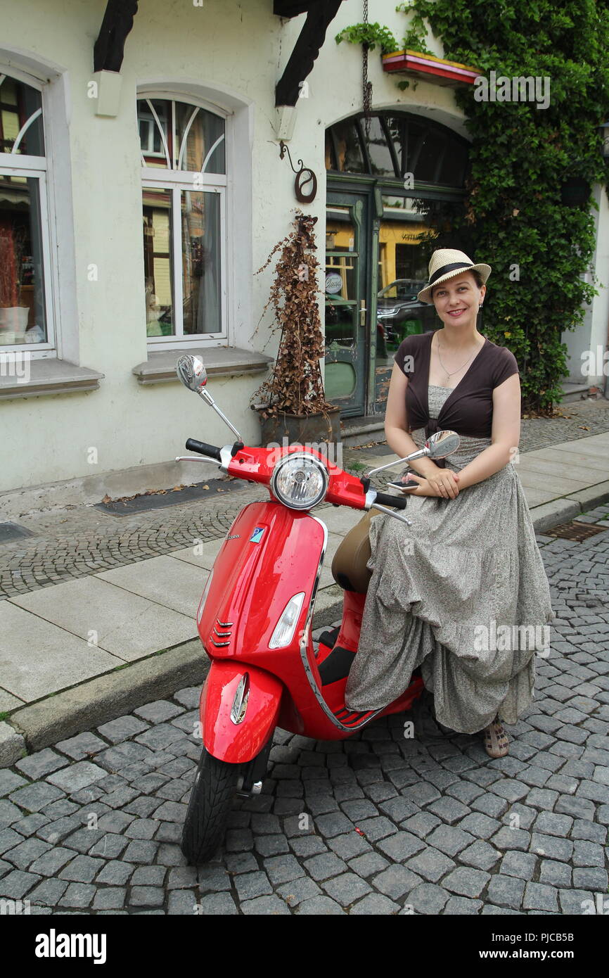 Junge Frau sitzt auf einem roten Roller. Stockfoto