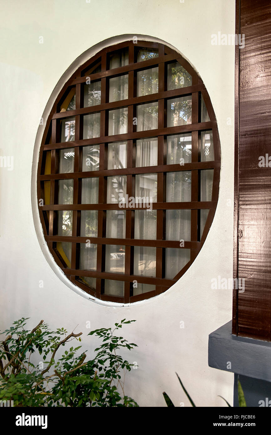 Japanisches Fenster. Rundes Fenster mit Holzpaneellen in einer weißen Wand Stockfoto