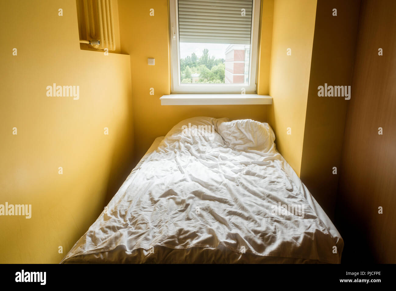 Schmale gelbe Schlafzimmer Innenraum mit Fenster Licht und zerknittert weisse Decke auf dem Bett Stockfoto