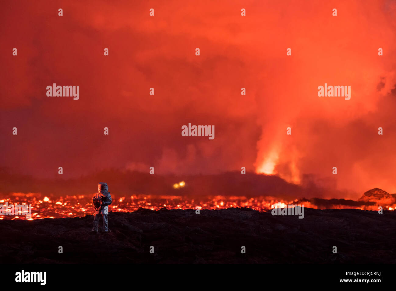 Ein Feuerwehrmann Tests Hitze Schutzbekleidung neben einem glühenden Fluss der heissen Lava ausbrechenden aus Spalte 8 (im Hintergrund) Der Kilauea East rift zone Stockfoto