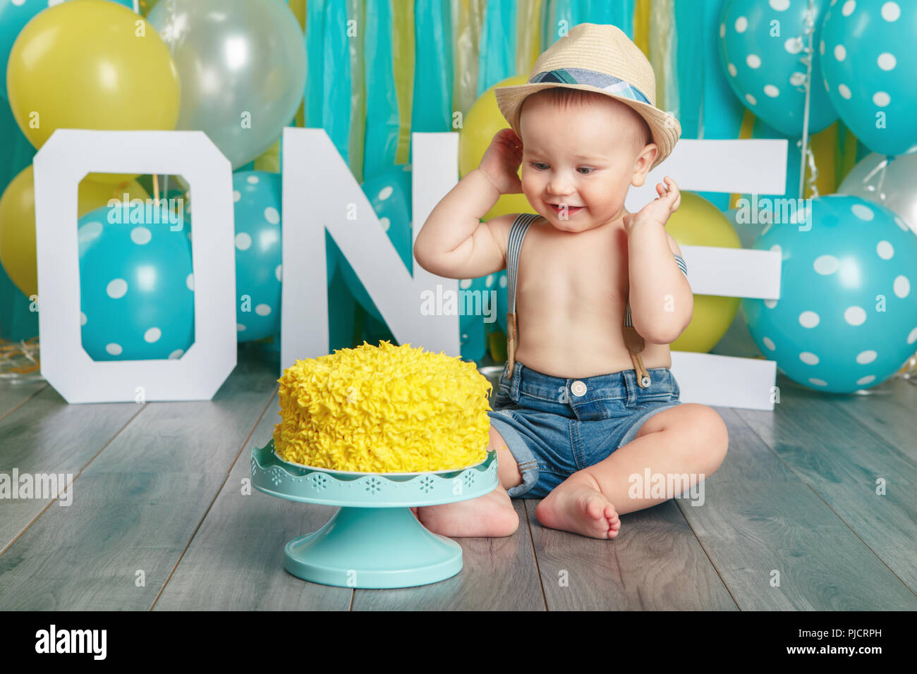 Portrait von cute adorable Kaukasische baby boy Jeans Hosen und hat seinen ersten Geburtstag feiert. Kuchen smash-Konzept. Kind sitzen auf Floo Stockfoto