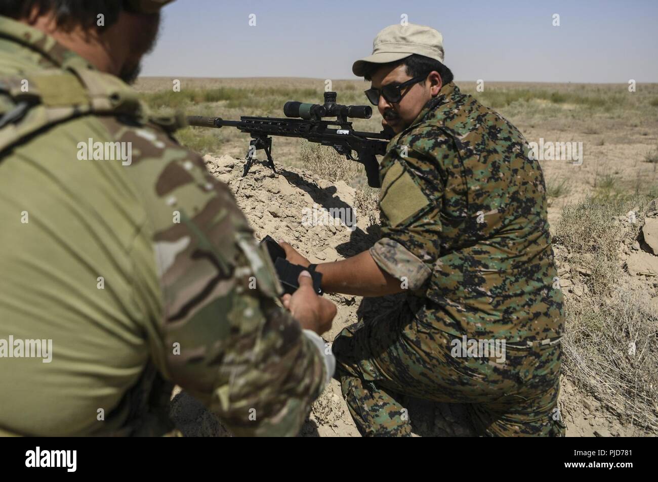 Eine Koalition Soldat Hände ein Magazin zu einem syrischen Demokratischen Kräfte Soldat während einer Live-fire Übung an einer Strecke in der Nähe von Dawr az Zawr, Syrien, 20. Juli 2018. Die Schulung ist Teil des gesamten Combined Joint Task Force-Operation inhärenten Building Partner Kapazität mission lösen, die darauf abzielt, die Kapazitäten der zusammengeschlossen, um Kräfte, die ISIS zu verbessern. CJTF-OIR ist die globale Koalition zu besiegen ISIS im Irak und in Syrien. Stockfoto