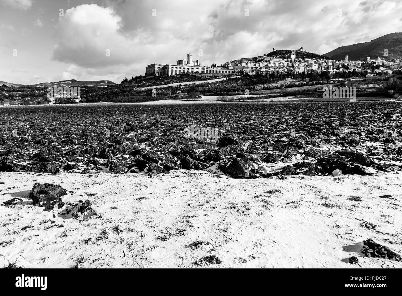 Blick auf die Stadt Assisi (Umbrien) im Winter, mit einem Feld durch Schnee und ein blauer Himmel mit weißen Wolken bedeckt Stockfoto