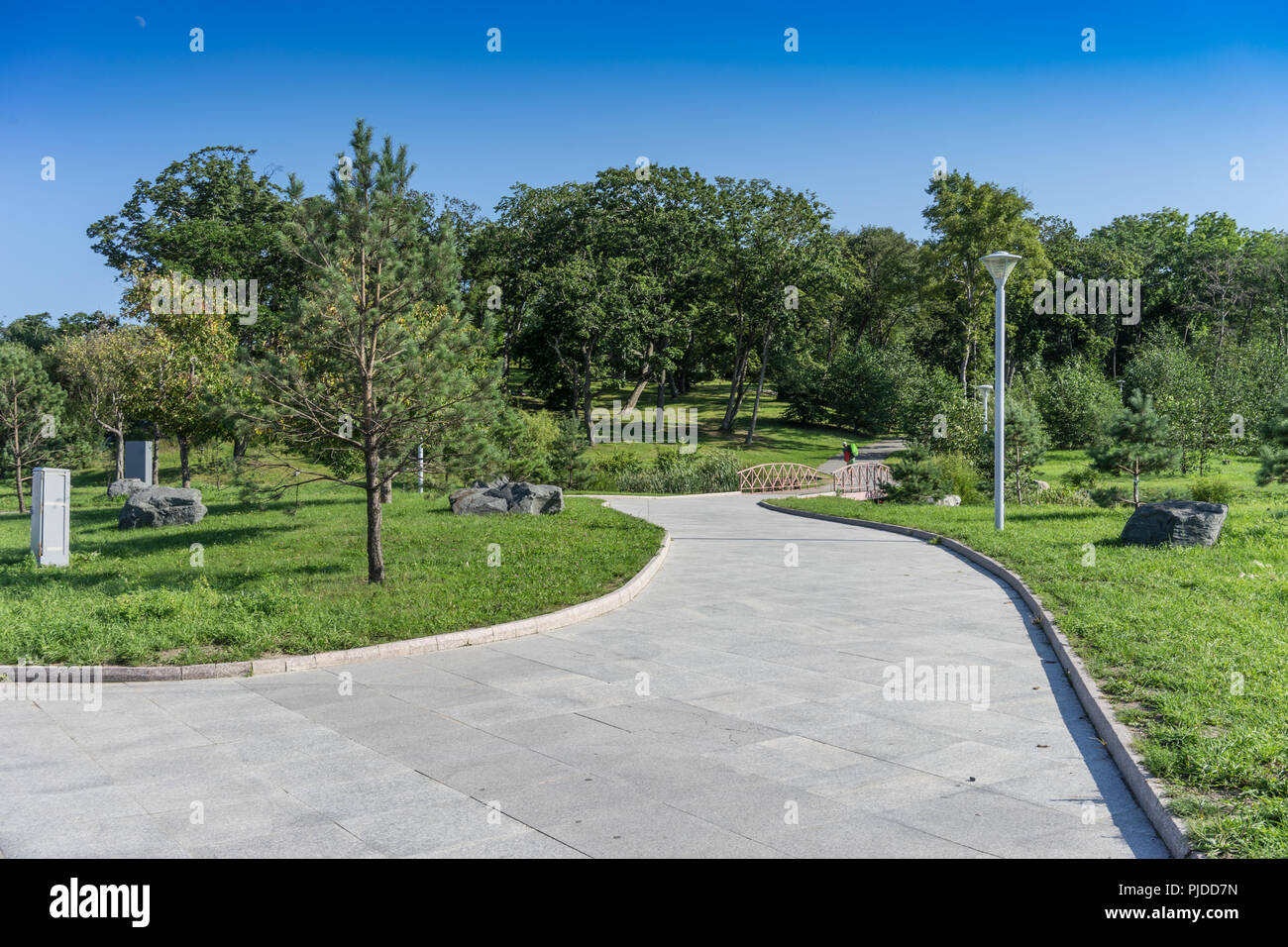 Ein Pfad in einem modernen, gepflegten Park mit grünen Bäumen und eine hölzerne Brücke. Wladiwostok, Russland Stockfoto