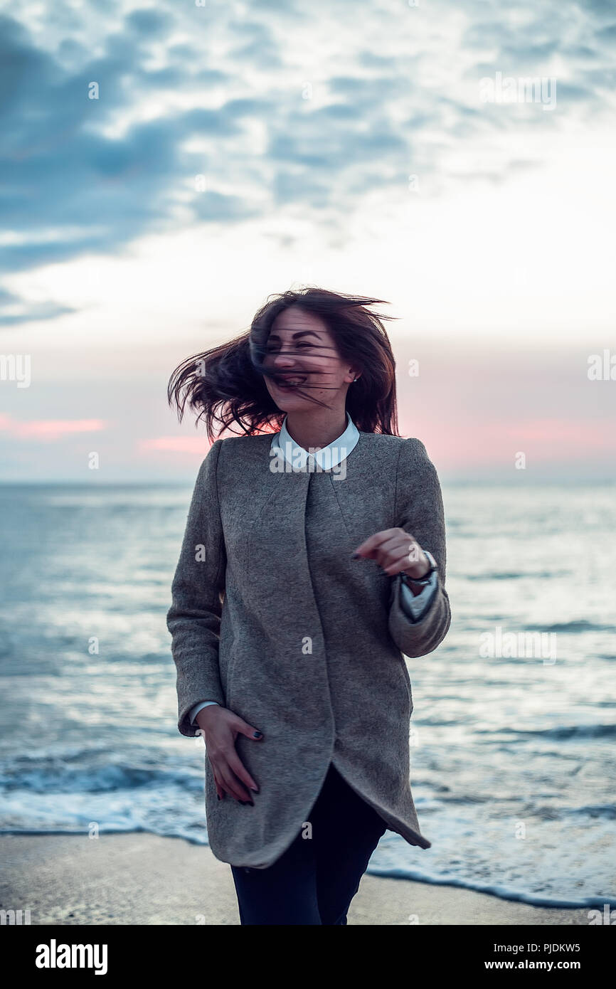 Porträt der jungen Frau, die am Strand, mit dem Rücken zum Meer, Wind Ihr Haar weht, lächelnd Stockfoto
