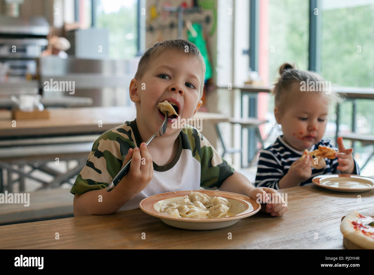 Kinder essen Pizza und Fleisch Knödel im Cafe. Kinder essen ungesundes Essen drinnen. Geschwister im Cafe, Familienurlaub Konzept. Stockfoto