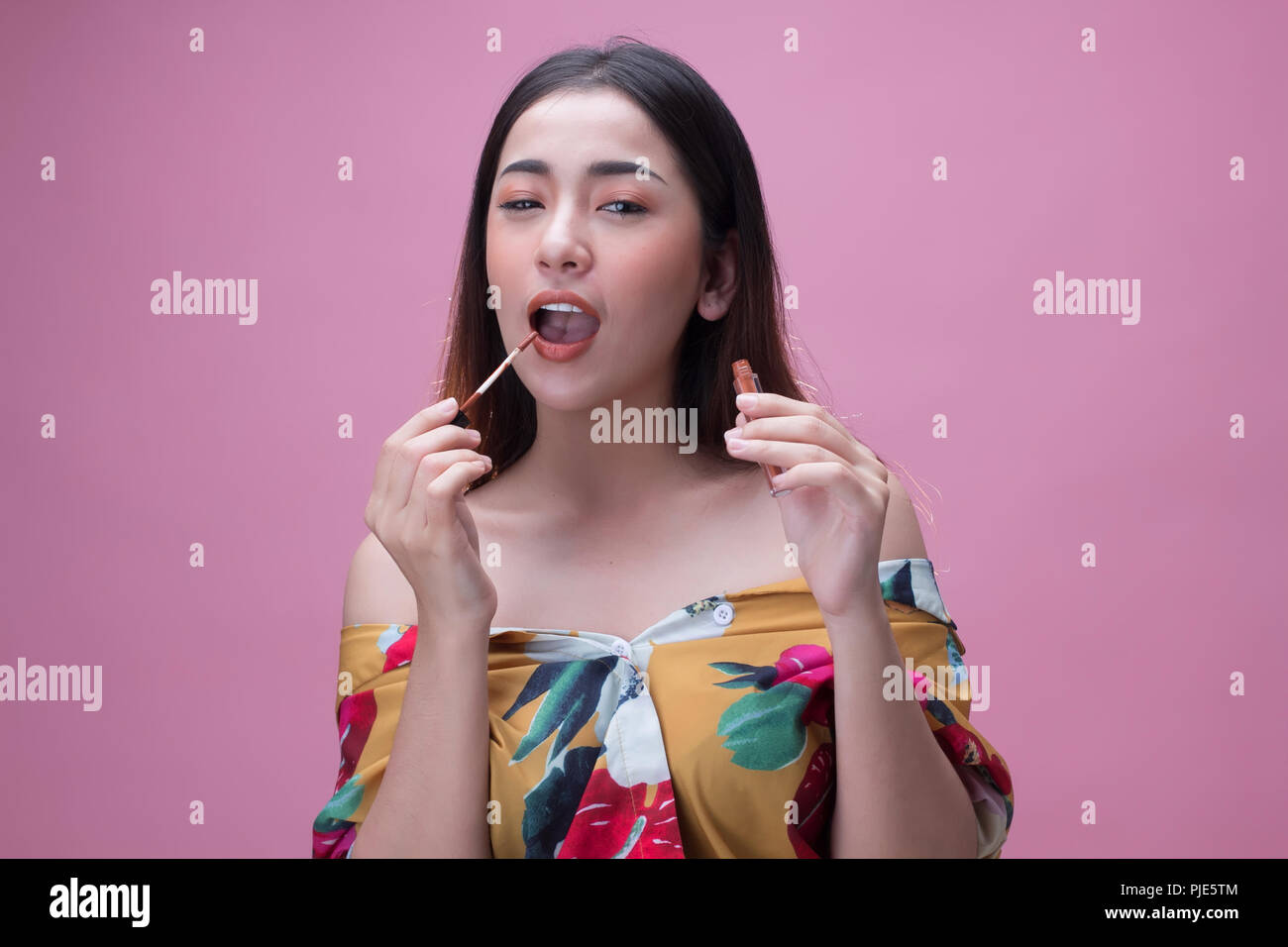 Junge asiatische Frau Anwendung Lippenstift auf ihren Lippen, auf rosa Hintergrund isoliert Stockfoto