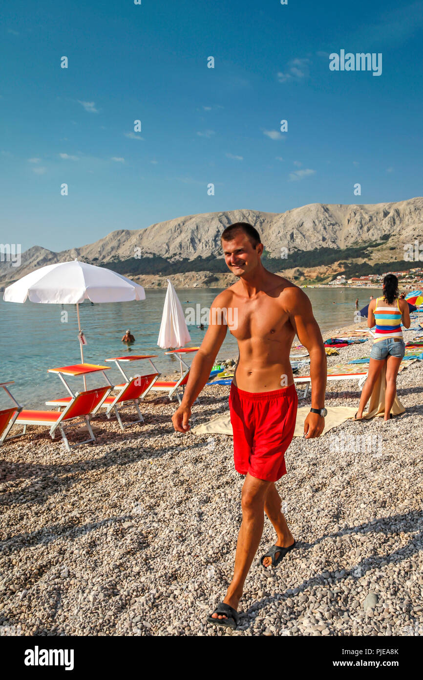 Schwimmer, Spaziergänger am Strand und Sonnenbaden am ruhigen Wasser der Adria auf der kroatischen Insel Krk, in der Kurstadt Baska Stockfoto