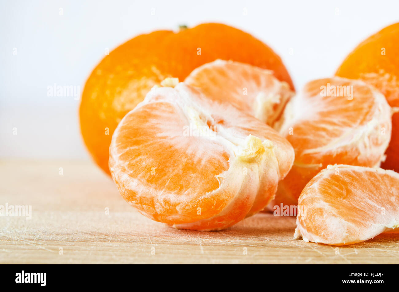 Der ganze, geschälte und segmentierten Satsumas, auf hellem Holz verkratzt alte Schneidbrett mit weisse Wand im Hintergrund. Stockfoto