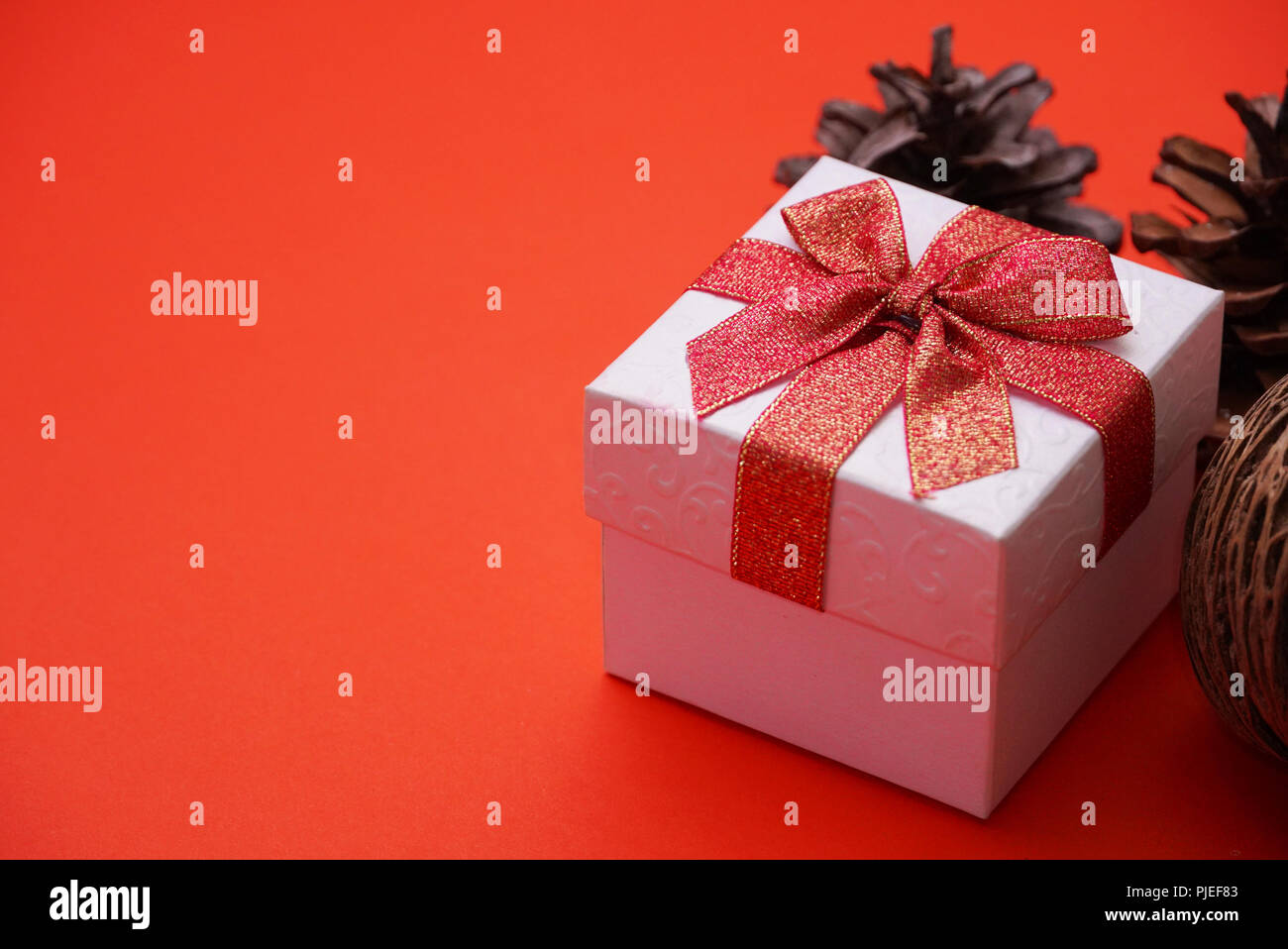 Weiß Geschenkbox mit roter Schleife und Pine Cone mit rotem Hintergrund und bieten Platz für die Idee. Stockfoto