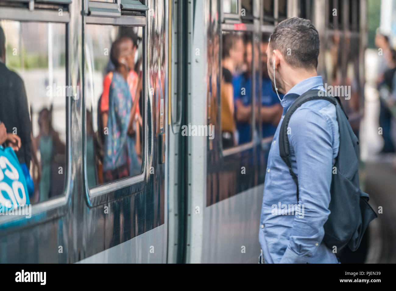 London, England - Juli 2018: der Mann, der das Hören von Musik über Kopfhörer beim Warten auf die S-Bahn anreisen, auf der Plattform, Großbritannien Stockfoto