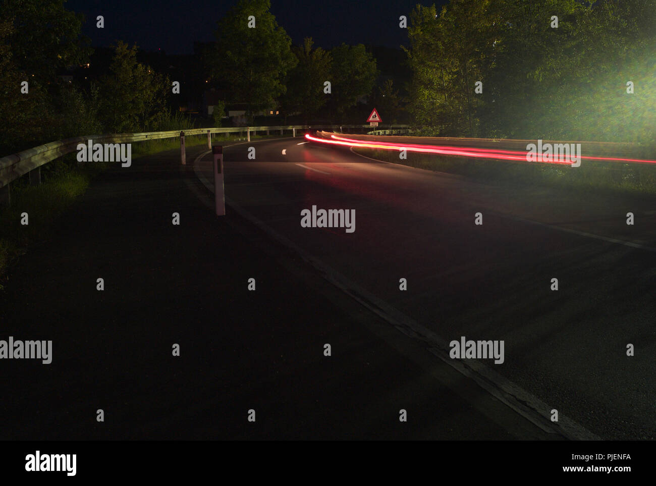 Verkehr in der Nacht - Rotes Licht Wanderwege rund um eine Landstraße Ecke - Lange Belichtung Stockfoto