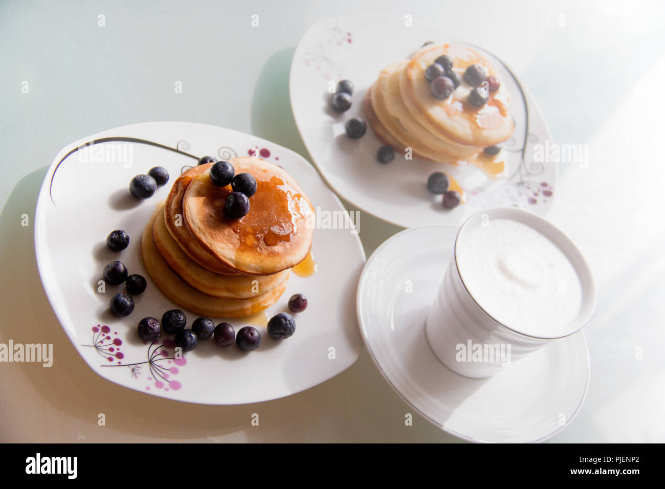 Hausgemachte Pfannkuchen Platten mit Ahornsirup, Zimt und Heidelbeeren auf weiße Platten mit Tasse köstlichen Kaffee mit Sahne garniert, süße Breakfas Stockfoto