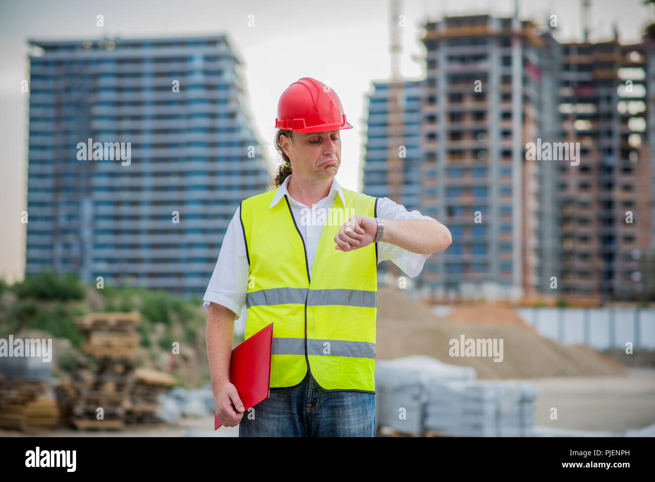 Ingenieur auf einer Baustelle auf seine Armbanduhr mit verschwommenen Gebäude im Hintergrund suchen Stockfoto