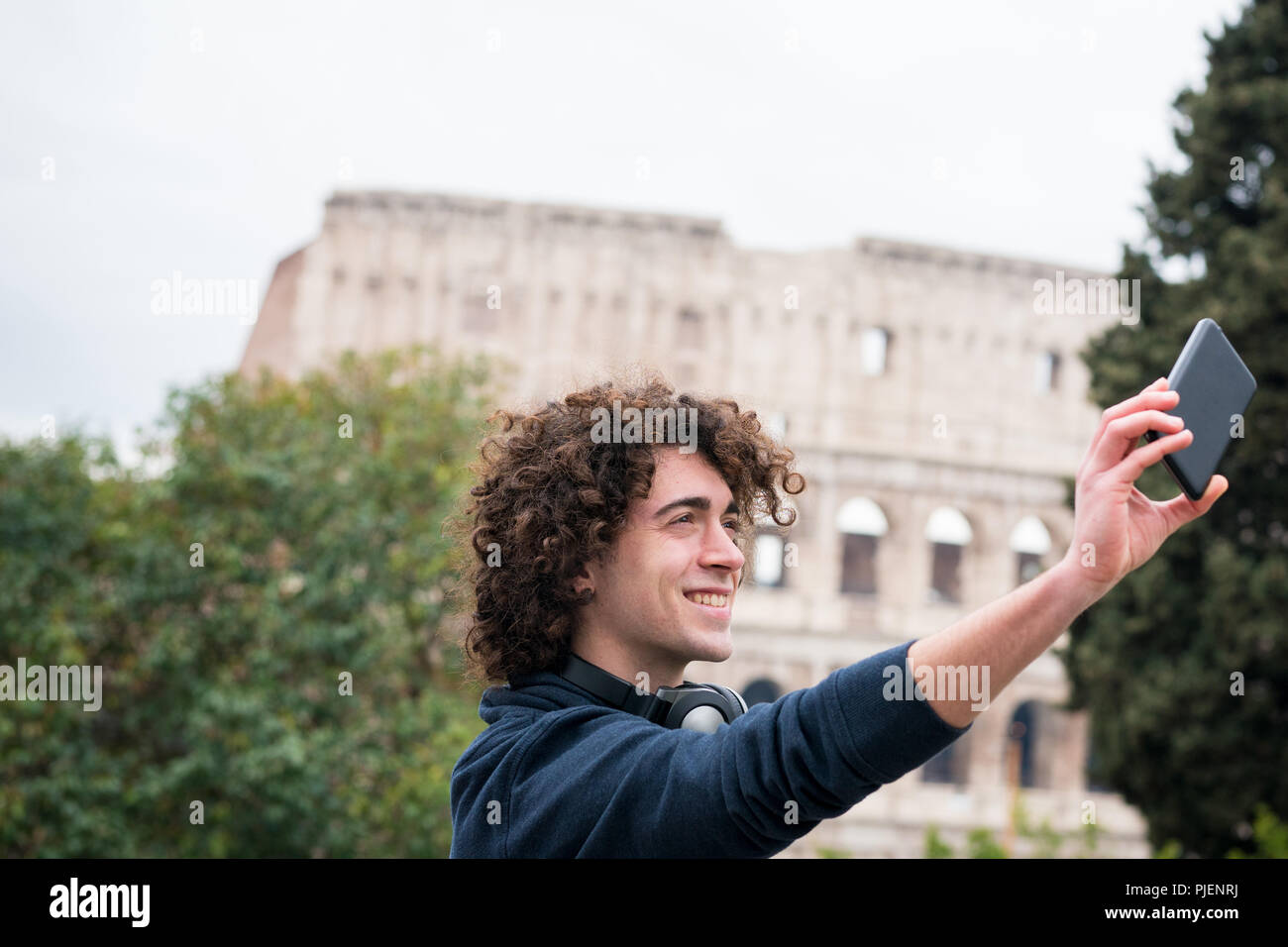Hübscher junger Mann mit lockigem Haar lächelnd und unter selfie mit seinem Handy Stockfoto