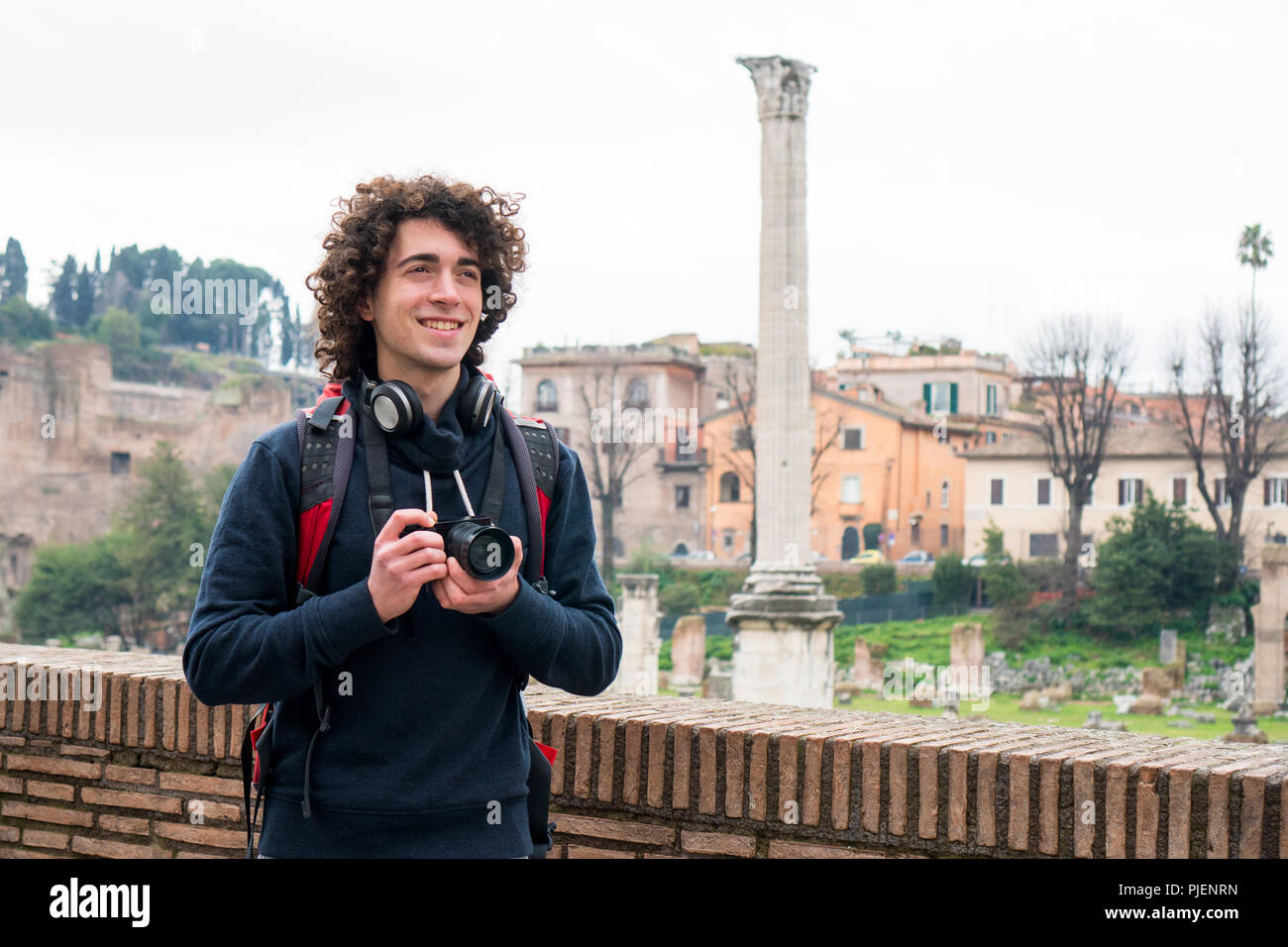 Hübscher junger Tourist mit lockigem Haar Fotos von Forum Romanum in Rom, Italien. Junger Mann mit seiner Kamera Stockfoto
