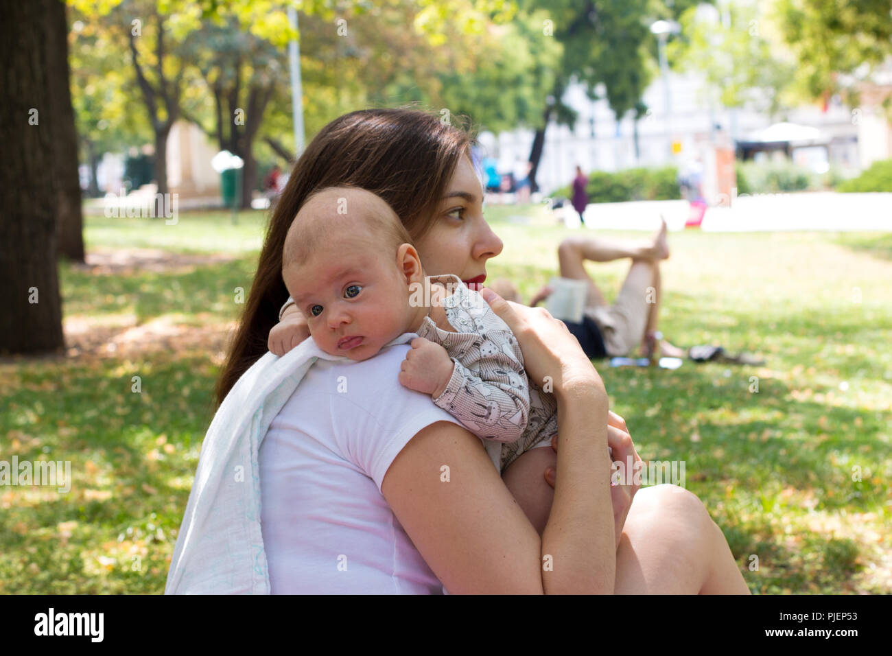 Mutter und Baby im öffentlichen Park, liebevolle Mutter Pflege niedliche Kind in die Hände nach dem Stillen, Baby's Kinn auf Mom Schulter aufstoßen Stockfoto