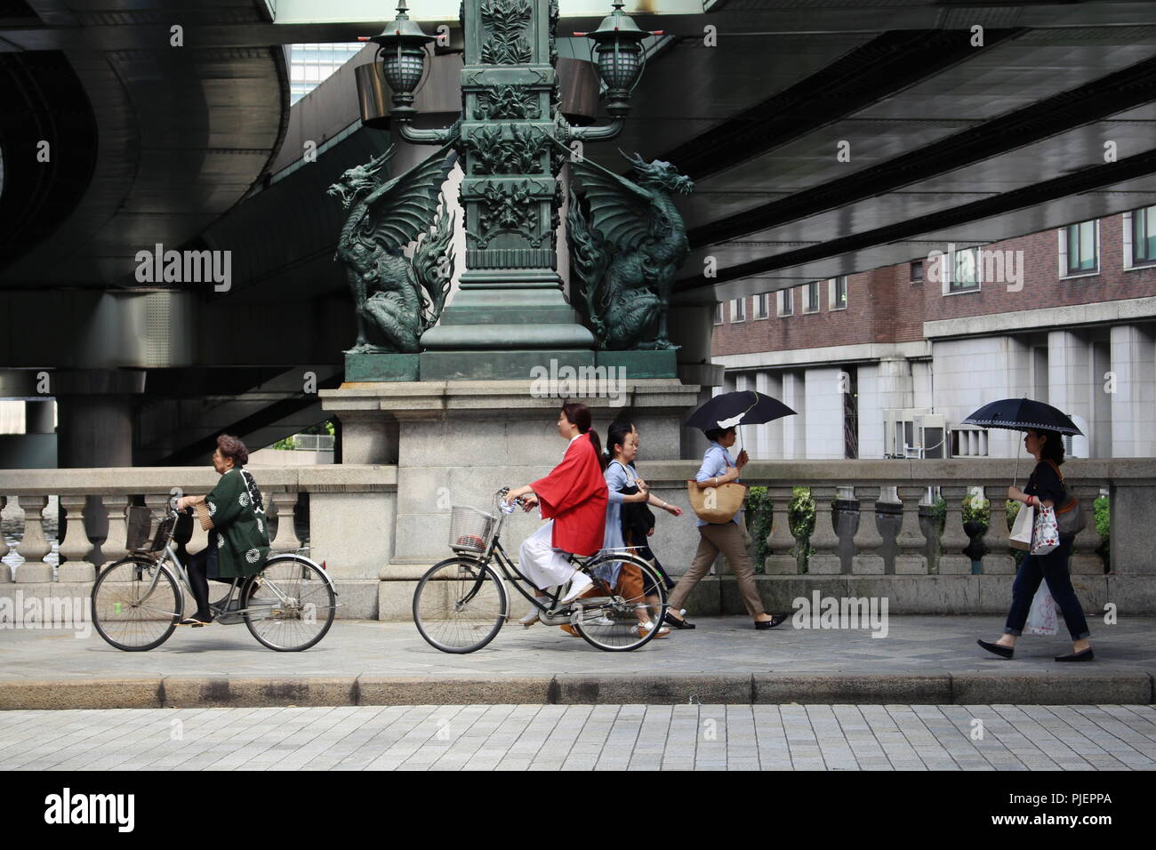 Fußgänger und Radfahrer pass Statuen von Drachen auf Nihonbashi Brücke. Die shoto Expressway ist oberhalb der Brücke. (Juni 2018) Stockfoto