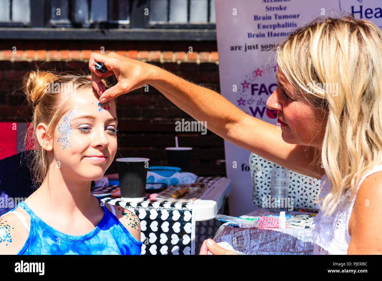 Kaukasischen jungen Teenager Mädchen, 12-13 Jahre alt, ihr Gesicht, blonde Frau in Abschaltstellung während der Veranstaltung gemalt haben. Pailletten zu Stirn angewendet. Stockfoto