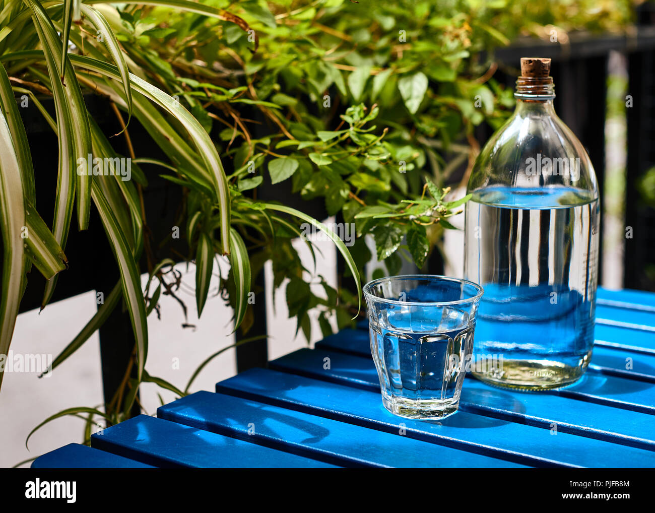 Das glas Flasche Trinkwasser auf dem blauen Tisch im sonnigen Tag Stockfoto