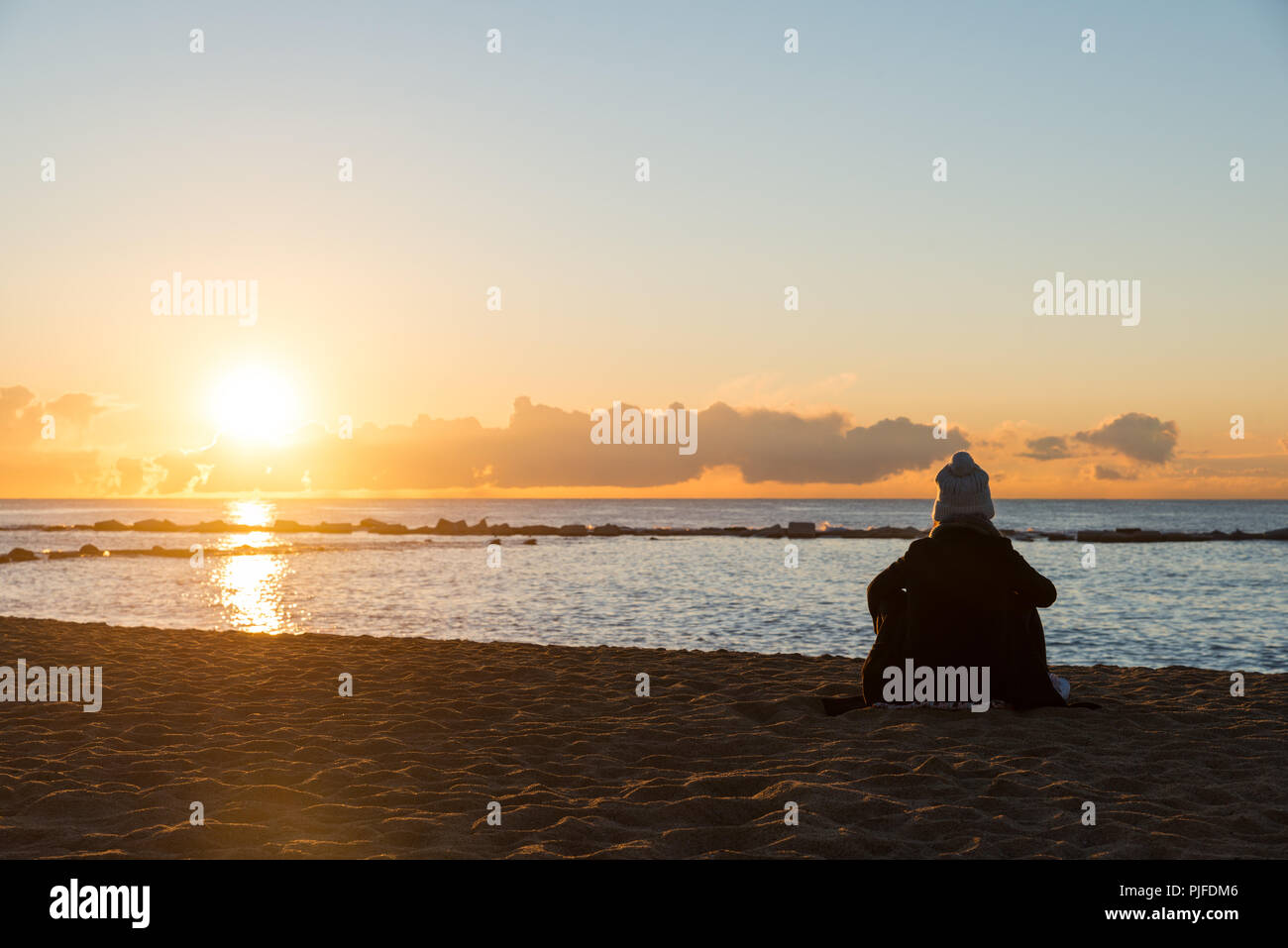 Glückliche Frau Sitzen auf kalten Strand mit Tasse Tee mit Beleuchtung bei Sonnenuntergang in Barcelona, Spanien. Stockfoto