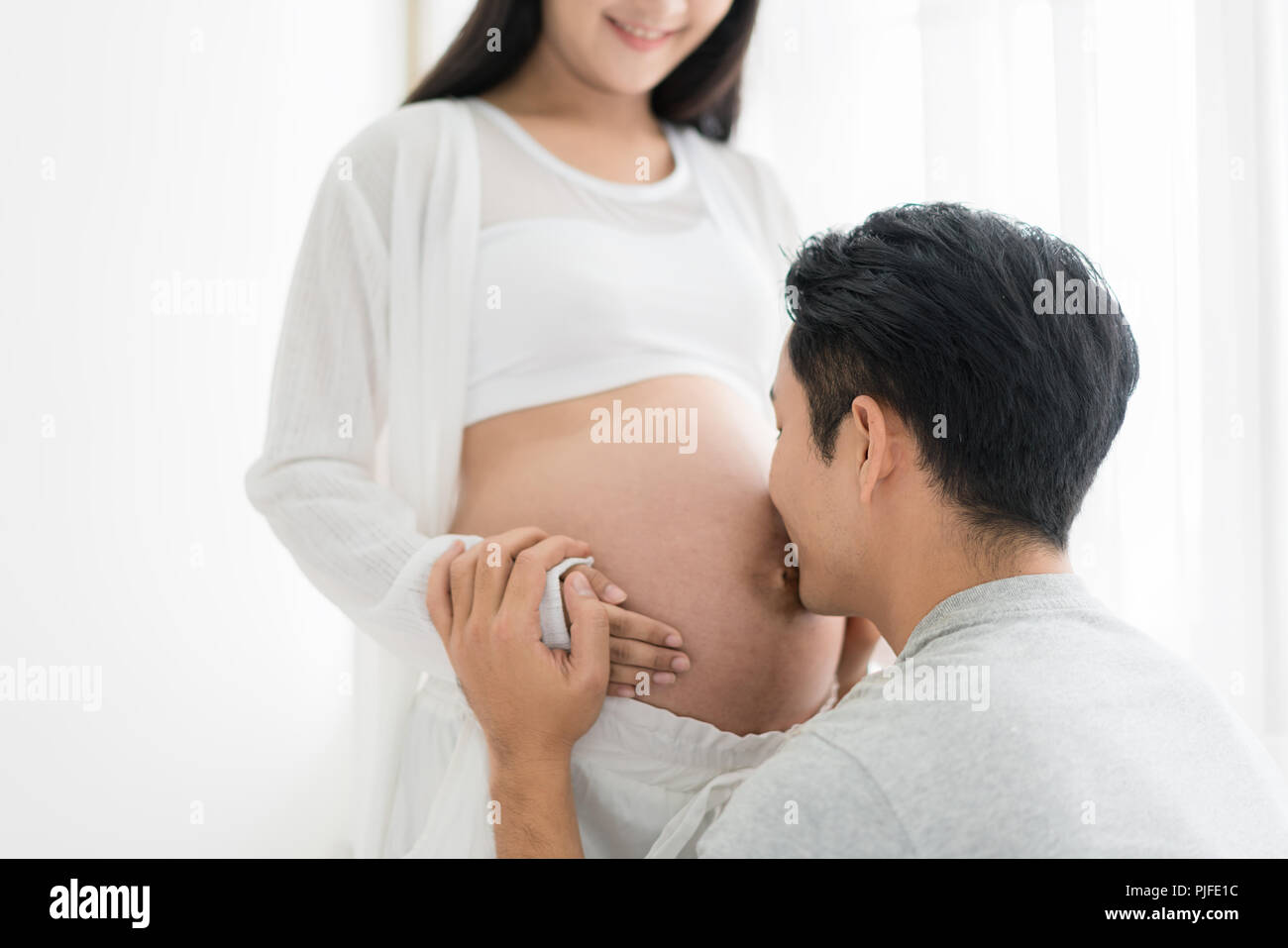 Asiatische Mann küssen schwanger Bauch seiner Frau mit geschlossenen Augen. Asiatische Ehepaar und Familie Konzept. Stockfoto