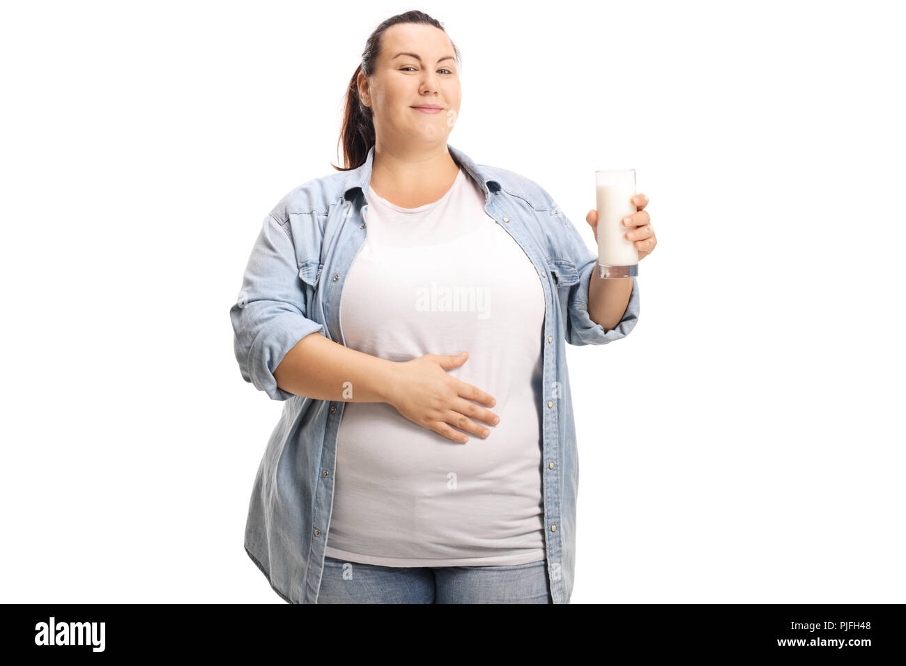 Zufrieden übergewichtige Frau mit einem Glas Milch ihre Hand auf ihren Bauch auf weißem Hintergrund Stockfoto