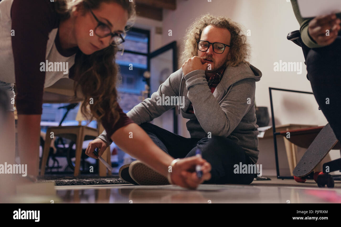 Team von tech Profis sitzen auf dem Boden und Brainstorming auf Neues Projekt planen. Frau schreiben Projektplan an Bord auf dem Boden mit Kollegen suchen Stockfoto