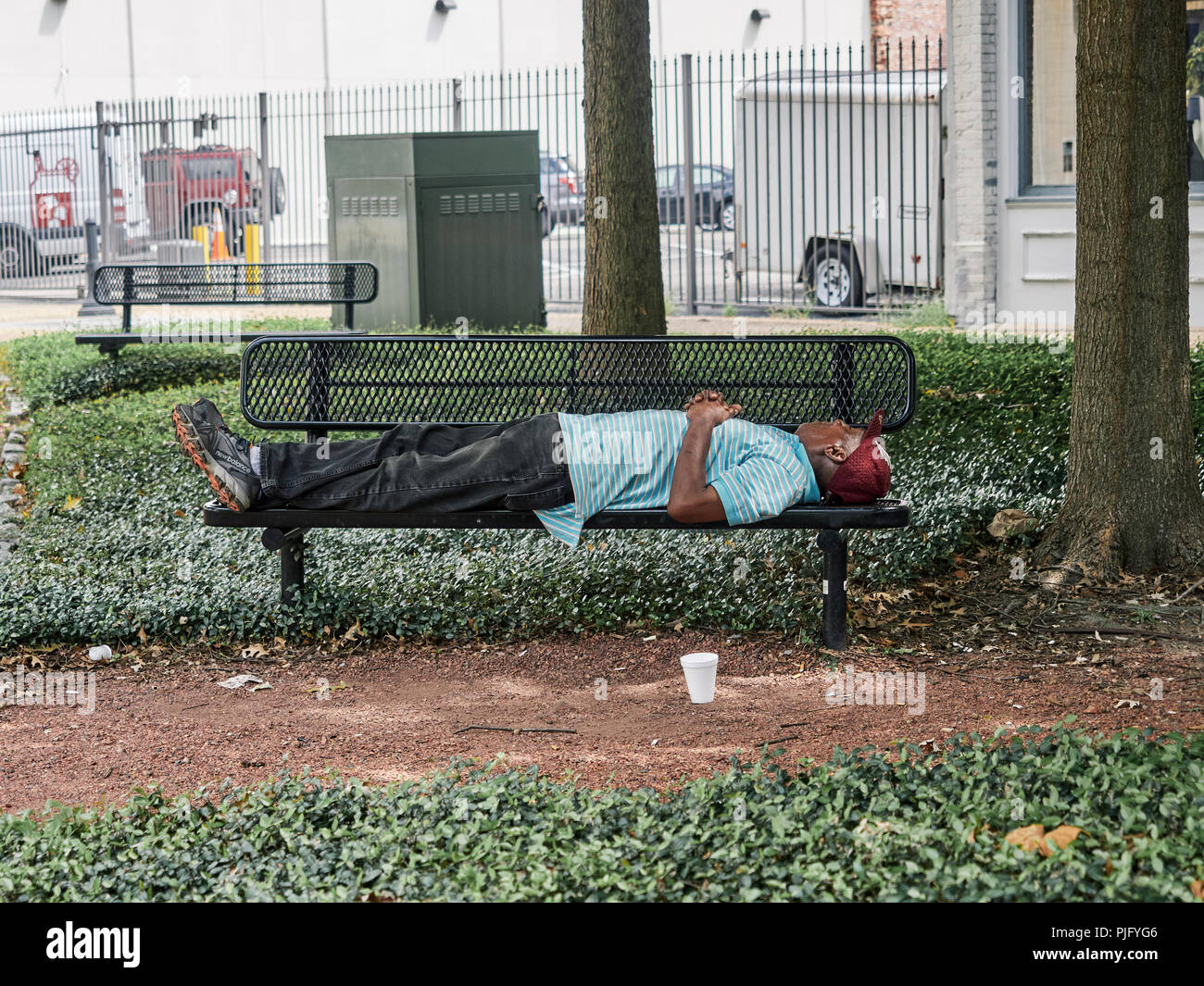 Obdachlosen afroamerikanischen oder schwarzer Mann auf einer Parkbank in Montgomery Alabama, USA schlafen. Stockfoto