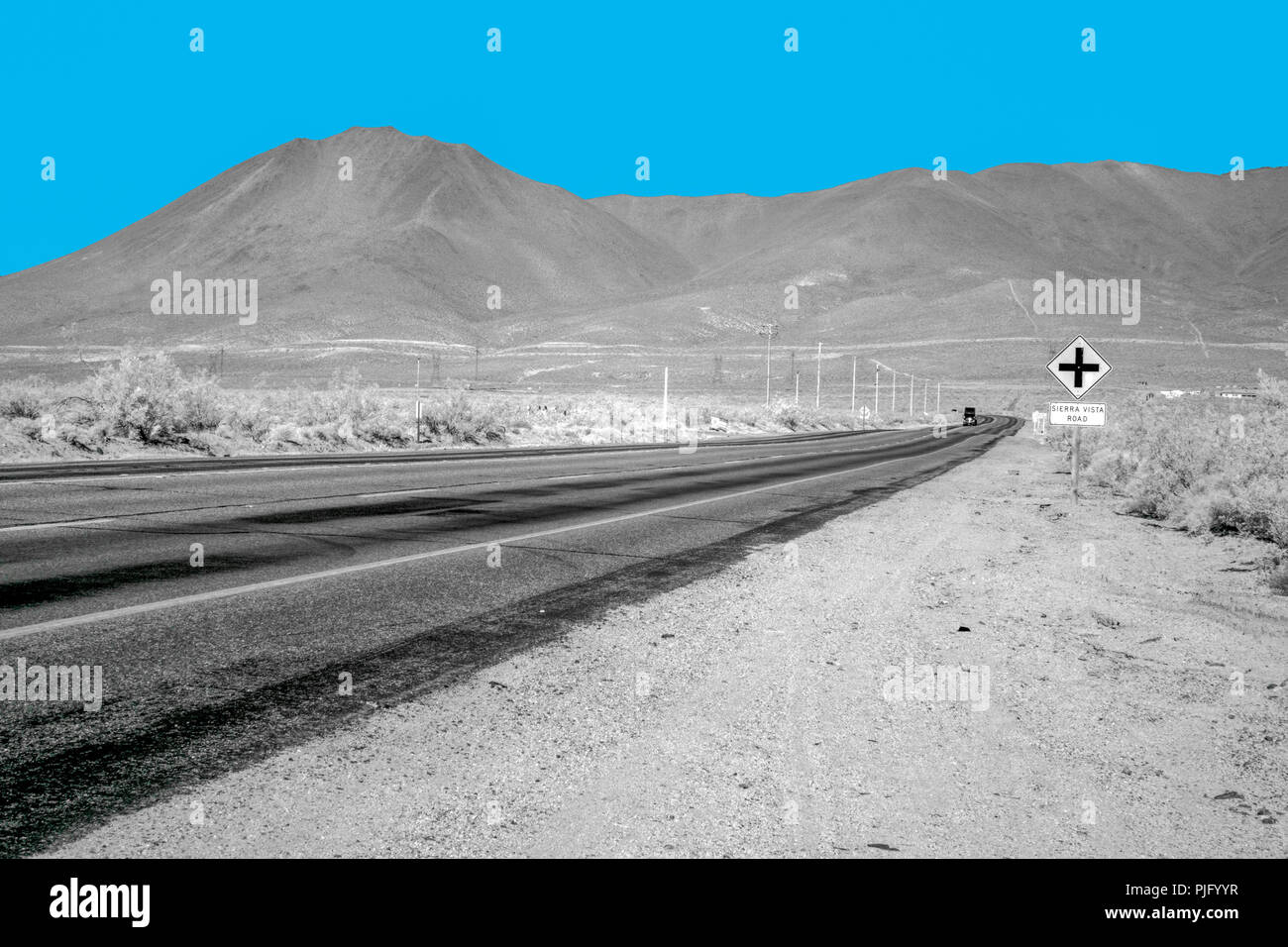 Einsame Wüste Autobahn in die kargen Berge unter einem strahlend blauen Himmel. Stockfoto