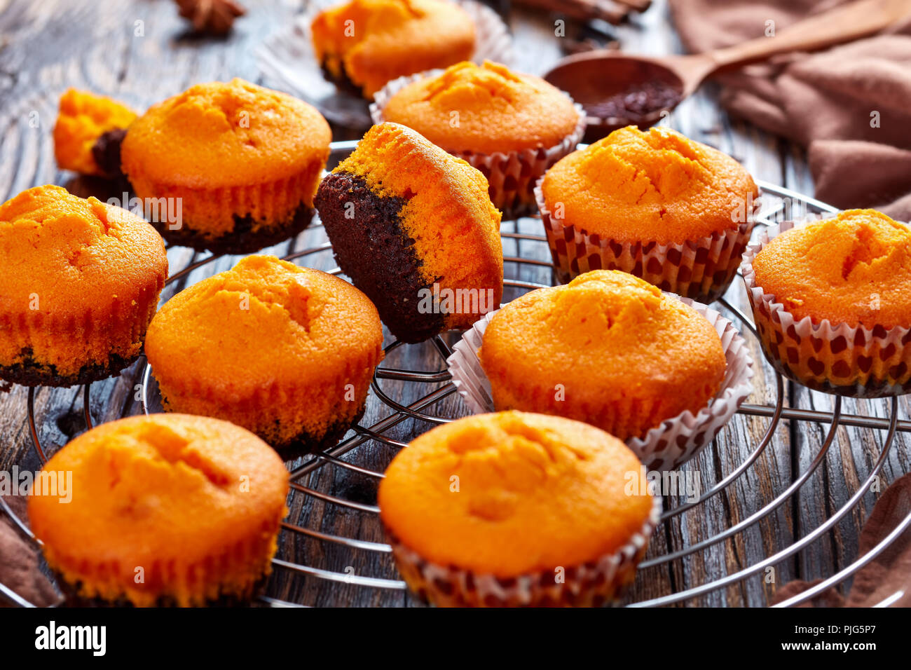 Frisch gebackene leckere Süße Kürbis Muffins auf einem runden Edelstahl Kuchen Kühlung Rack auf einem rustikalen Holztisch, leckere Herbst Dessert für Hal Stockfoto