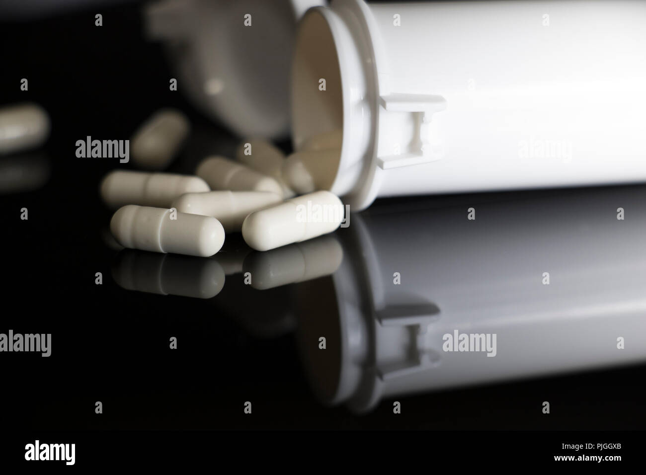 Weiße Pillen fallen um eine offene Pille Container auf einem schwarzen, glänzenden Oberfläche. Geöffnete Flasche verschreibungspflichtige Pillen mit Medizin fallen von oben. Stockfoto