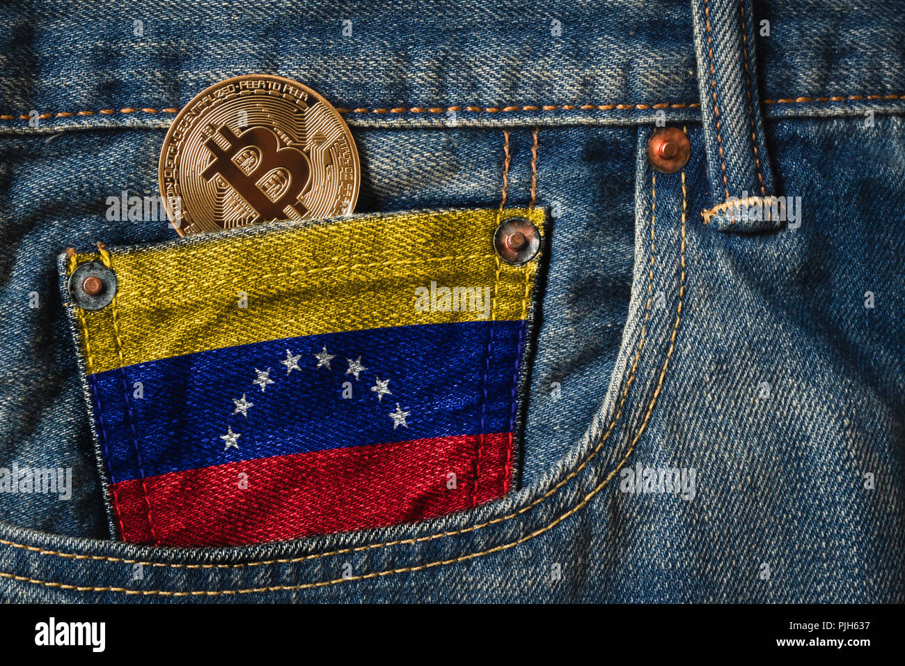 Golden BITCOIN (BTC) cryptocurrency in der Tasche der Jeans mit der Flagge der Bolivarischen Republik Venezuela auf Jeans Denim Textur. Stockfoto