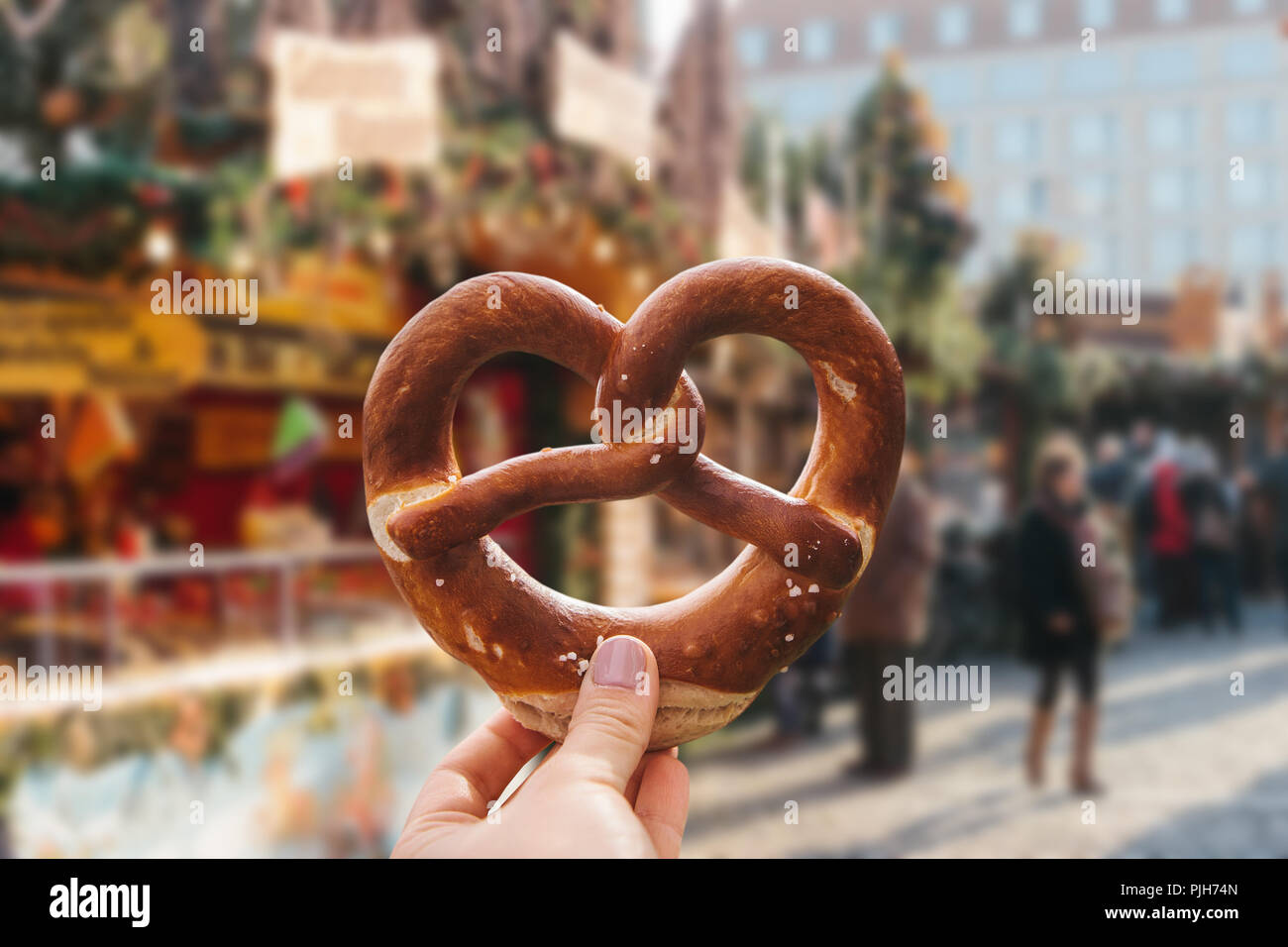 Das Mädchen ist eine traditionelle deutsche Brezel in der Hand. Weihnachtsmarkt im Hintergrund. Stockfoto