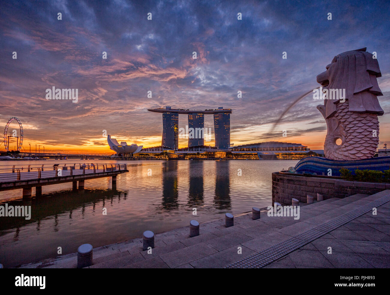Skyline von Singapur bei Sonnenaufgang, mit der Merlion, das Marina Bay Sands, der Kunst und Wissenschaft Museum und der Singapore Flyer, alle unter einem dramatischen Himmel. Stockfoto