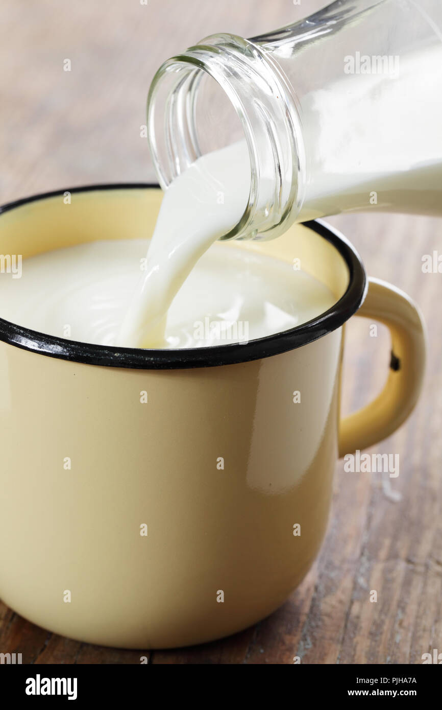 Gießen Milch in der rustikalen Emaille Tasse Stockfoto