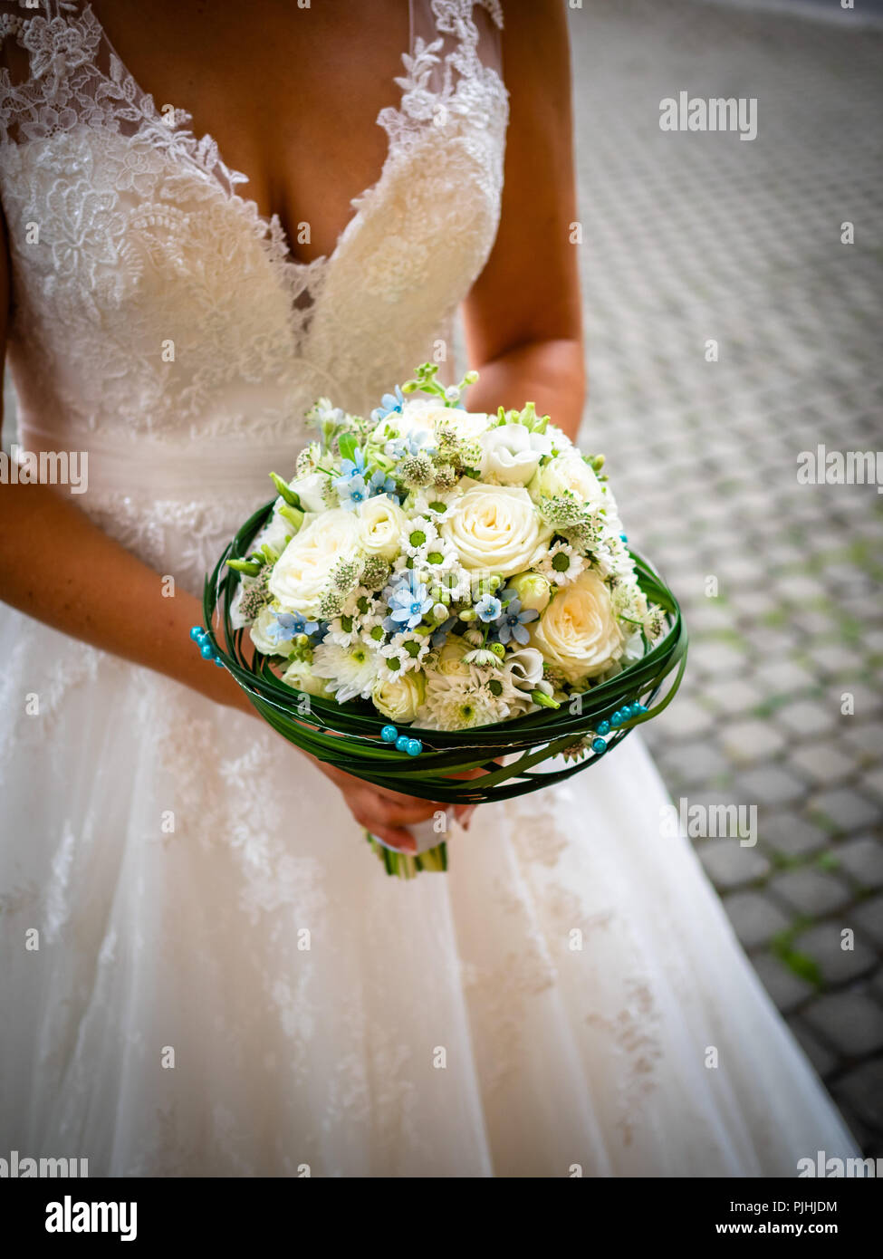 Die Braut hält den Strauß mit weißen Rosen und kleinen blauen Blumen, mit  grünen Blättern und blauen Perlen umgeben, weiße Spitzen Kleid, und  Gänseblümchen Stockfotografie - Alamy
